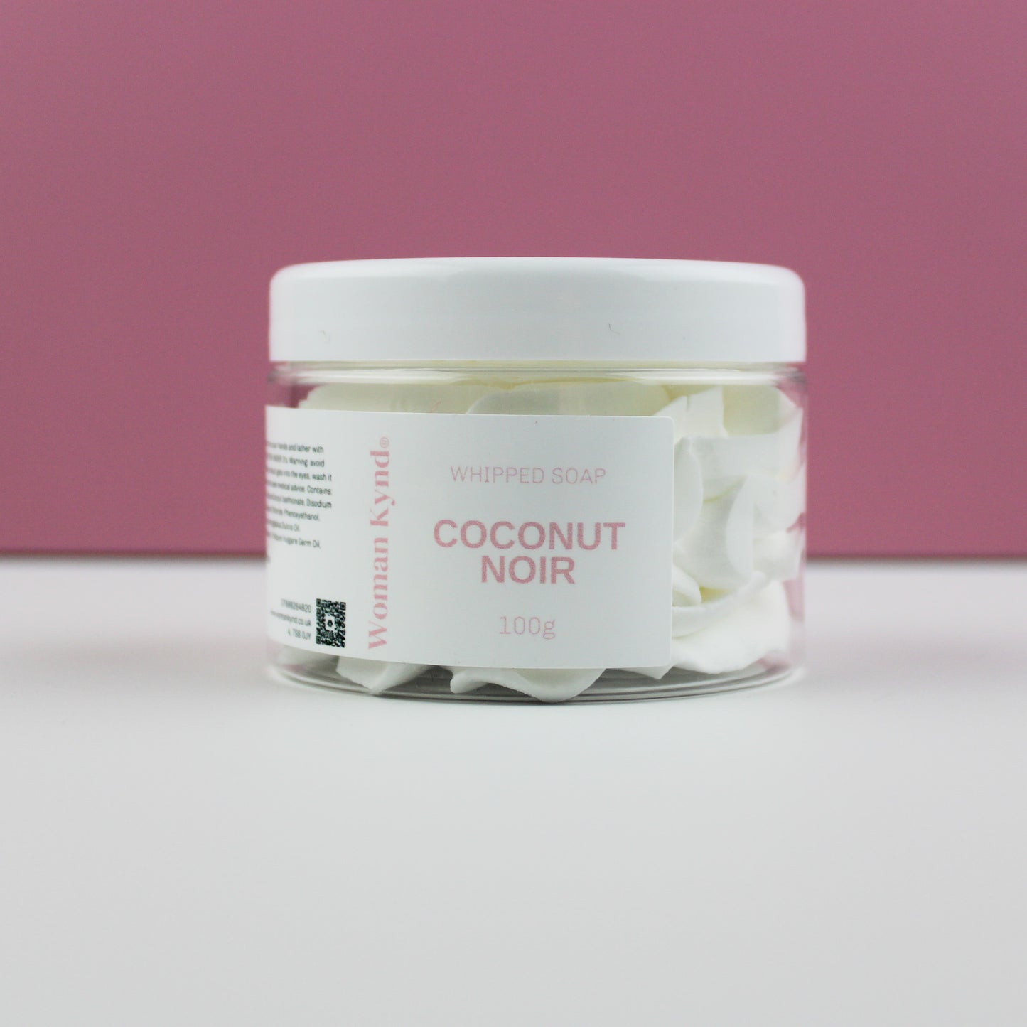 A jar of Coconut Noir Whipped Soap by Woman Kynd set against a pink background.