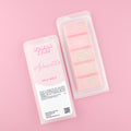 Two images of a Woman Kynd five segment pink Wax Melt with gold glitter, both in a frosted clamshell. The first image displays the pink and white label with the words Woman Kynd Aphrodite Wax Melt and the CLP information, and the other image is of the reverse side showing the Wax Melt Itself. Both images are against a solid pink background.