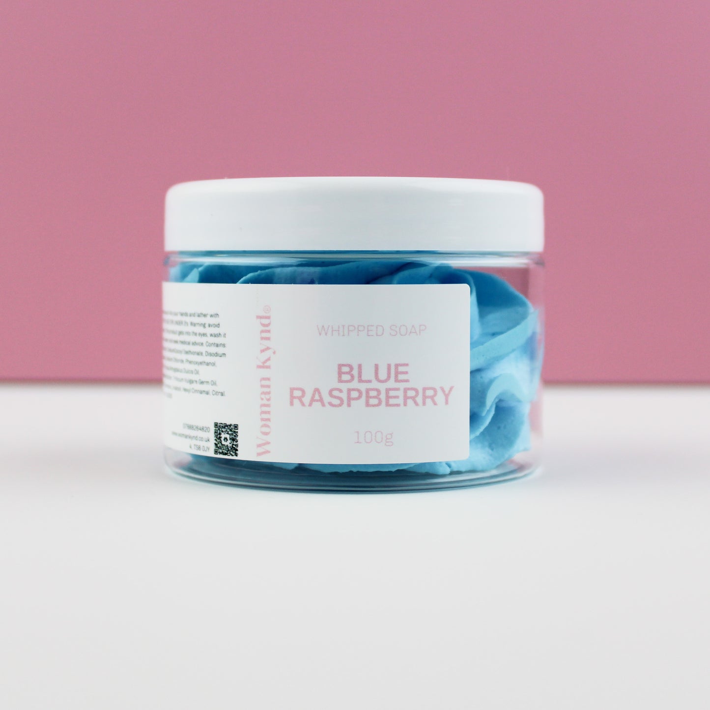 A clear jar filled with blue whipped soap, labeled 'Blue Raspberry' on a pink background.