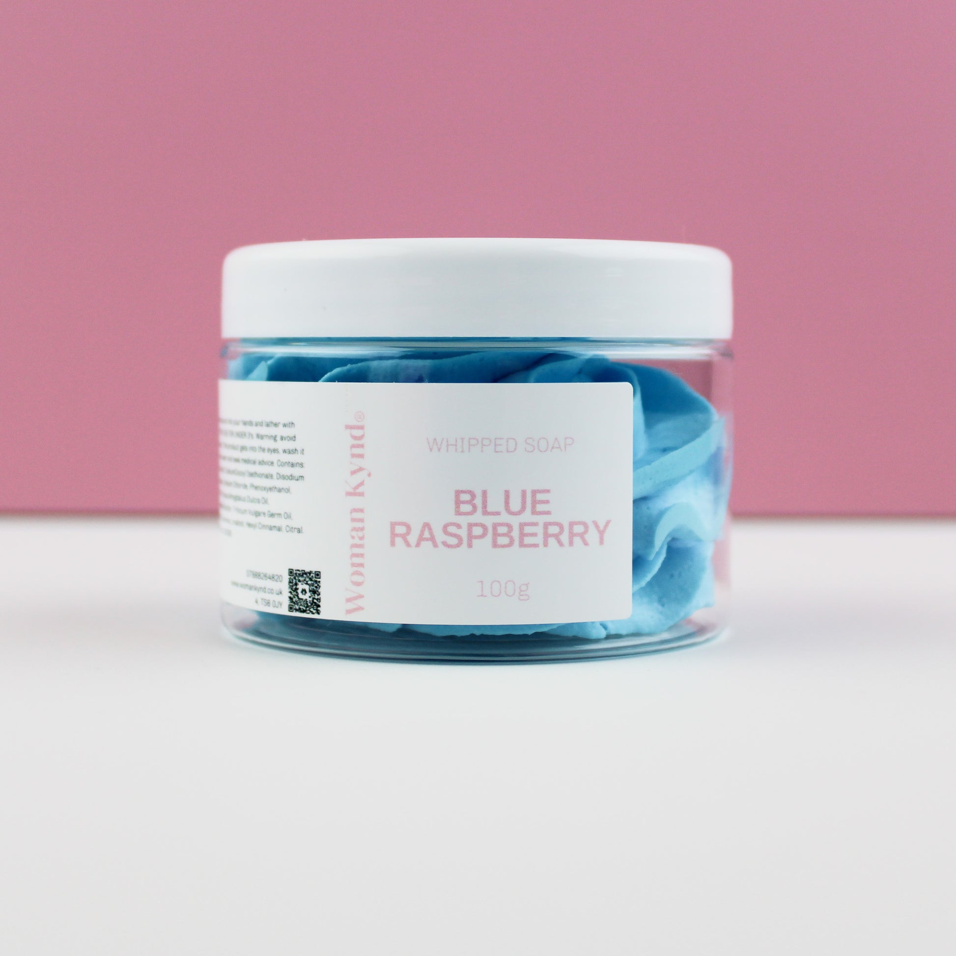 A clear jar filled with blue whipped soap, labeled 'Blue Raspberry' on a pink background.
