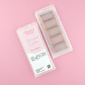 Two images of a Woman Kynd five segment light brown Wax Melt with dark brown glitter, both in a frosted clamshell. The first image displays the pink and white label with the words Woman Kynd Caramel dates Wax Melt and the CLP information, and the other image is of the reverse side showing the Wax Melt Itself. Both images are against a solid pink background.