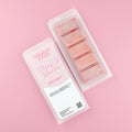 Two images of a Woman Kynd five segment red Wax Melt with gold glitter, both in a frosted clamshell. The first image displays the pink and white label with the words Woman Kynd Cherry & Vanilla Wax Melt and the CLP information, and the other image is of the reverse side showing the Wax Melt Itself. Both images are against a solid pink background.