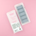 Two images of a Woman Kynd five segment black Wax Melt with black glitter, both in a frosted clamshell. The first image displays the pink and white label with the words Woman Kynd Coconut Noir Wax Melt and the CLP information, and the other image is of the reverse side showing the Wax Melt Itself. Both images are against a solid pink background.