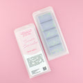 Two images of a Woman Kynd five segment purple Wax Melt with green glitter, both in a frosted clamshell. The first image displays the pink and white label with the words Woman Kynd Cosmic Encounter Wax Melt and the CLP information, and the other image is of the reverse side showing the Wax Melt Itself. Both images are against a solid pink background.