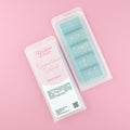 Two images of a Woman Kynd five segment aqua blue Wax Melt with gold glitter, both in a frosted clamshell. The first image displays the pink and white label with the words Woman Kynd Downtown Dubai Wax Melt and the CLP information, and the other image is of the reverse side showing the Wax Melt Itself. Both images are against a solid pink background.