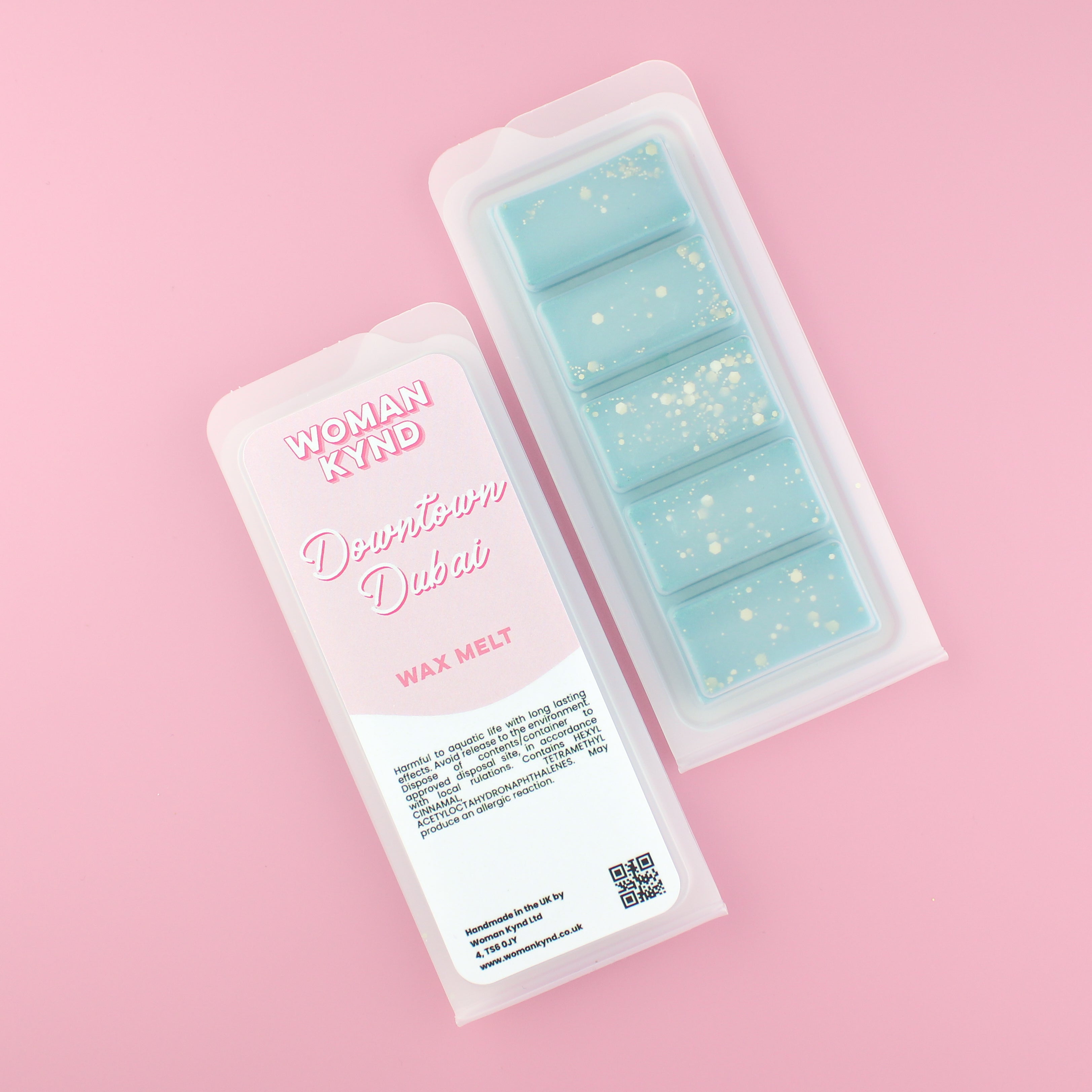 Two images of a Woman Kynd five segment aqua blue Wax Melt with gold glitter, both in a frosted clamshell. The first image displays the pink and white label with the words Woman Kynd Downtown Dubai Wax Melt and the CLP information, and the other image is of the reverse side showing the Wax Melt Itself. Both images are against a solid pink background.