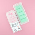 Two images of a Woman Kynd five segment mint green Wax Melt with white, snowflake shaped glitter, both in a frosted clamshell. The first image displays the pink and white label with the words Woman Kynd Frosted Eucalyptus Wax Melt and the CLP information, and the other image is of the reverse side showing the Wax Melt Itself. Both images are against a solid pink background.