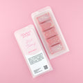 Two images of a Woman Kynd five segment red Wax Melt with gold glitter, both in a frosted clamshell. The first image displays the pink and white label with the words Woman Kynd Hot Cherry Wax Melt and the CLP information, and the other image is of the reverse side showing the Wax Melt Itself. Both images are against a solid pink background.