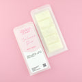 Two images of a Woman Kynd five segment beigeWax Melt with off-white glitter, both in a frosted clamshell. The first image displays the pink and white label with the words Woman Kynd Cashmere Glow Wax Melt and the CLP information, and the other image is of the reverse side showing the Wax Melt Itself. Both images are against a solid pink background.