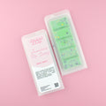 Two images of a Woman Kynd five segment green Wax Melt with black and yellow glitter, both in a frosted clamshell. The first image displays the pink and white label with the words Woman Kynd Jamaican Me Crazy Wax Melt and the CLP information, and the other image is of the reverse side showing the Wax Melt Itself. Both images are against a solid pink background.
