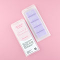 Two images of a Woman Kynd five segment purple Wax Melt with silver glitter, both in a frosted clamshell. The first image displays the pink and white label with the words Woman Kynd Lavender & Marshmallow Wax Melt and the CLP information, and the other image is of the reverse side showing the Wax Melt Itself. Both images are against a solid pink background.