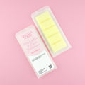 Two images of a Woman Kynd five segment pale yellow Wax Melt with white glitter, both in a frosted clamshell. The first image displays the pink and white label with the words Woman Kynd Marshmallow & Lemon Buttercream Wax Melt and the CLP information, and the other image is of the reverse side showing the Wax Melt Itself. Both images are against a solid pink background.