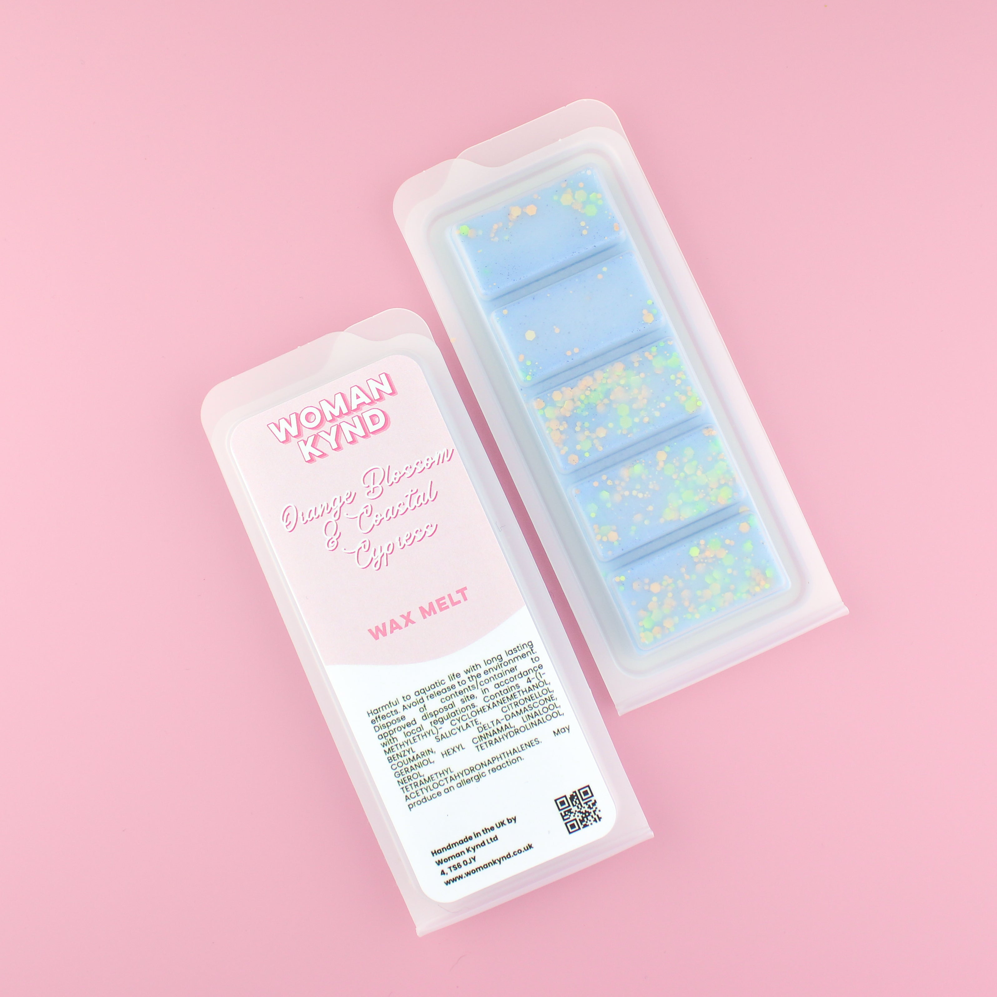 Two images of a Woman Kynd five segment light blue Wax Melt with yellow and green glitter, both in a frosted clamshell. The first image displays the pink and white label with the words Woman Kynd Orange Blossom & Coastal Cypress Wax Melt and the CLP information, and the other image is of the reverse side showing the Wax Melt Itself. Both images are against a solid pink background.