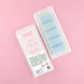 Two images of a Woman Kynd five segment pale blue Wax Melt with gold glitter, both in a frosted clamshell. The first image displays the pink and white label with the words Woman Kynd Oud Mirage Wax Melt and the CLP information, and the other image is of the reverse side showing the Wax Melt Itself. Both images are against a solid pink background.