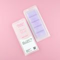 Two images of a Woman Kynd five segment pale purple Wax Melt with pale purple glitter, both in a frosted clamshell. The first image displays the pink and white label with the words Woman Kynd Parma Violet Wax Melt and the CLP information, and the other image is of the reverse side showing the Wax Melt Itself. Both images are against a solid pink background.