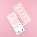 Two images of a Woman Kynd five segment pale pink Wax Melt with white glitter, both in a frosted clamshell. The first image displays the pink and white label with the words Woman Kynd Pink Shores Wax Melt and the CLP information, and the other image is of the reverse side showing the Wax Melt Itself. Both images are against a solid pink background.
