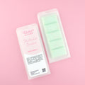 Two images of a Woman Kynd five segment pale green Wax Melt with gold glitter, both in a frosted clamshell. The first image displays the pink and white label with the words Woman Kynd Pistachio Sundae Wax Melt and the CLP information, and the other image is of the reverse side showing the Wax Melt Itself. Both images are against a solid pink background.