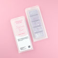 Two images of a Woman Kynd five segment light purple Wax Melt with silver glitter, both in a frosted clamshell. The first image displays the pink and white label with the words Woman Kynd Pyjama Time Wax Melt and the CLP information, and the other image is of the reverse side showing the Wax Melt Itself. Both images are against a solid pink background.