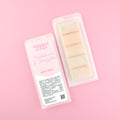 Two images of a Woman Kynd five segment beige Wax Melt with pale green glitter, both in a frosted clamshell. The first image displays the pink and white label with the words Woman Kynd Sandalwood & Eucalyptus Wax Melt and the CLP information, and the other image is of the reverse side showing the Wax Melt Itself. Both images are against a solid pink background.