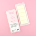Two images of a Woman Kynd five segment cream coloured Wax Melt with white glitter, both in a frosted clamshell. The first image displays the pink and white label with the words Woman Kynd Sea Shells Wax Melt and the CLP information, and the other image is of the reverse side showing the Wax Melt Itself. Both images are against a solid pink background.