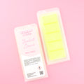 Two images of a Woman Kynd five segment fluorescent yellow Wax Melt with yellow glitter, both in a frosted clamshell. The first image displays the pink and white label with the words Woman Kynd Sherbet Lemon Wax Melt and the CLP information, and the other image is of the reverse side showing the Wax Melt Itself. Both images are against a solid pink background.