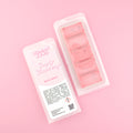 Two images of a Woman Kynd five segment pale red Wax Melt with red glitter, both in a frosted clamshell. The first image displays the pink and white label with the words Woman Kynd Simply Strawberry Wax Melt and the CLP information, and the other image is of the reverse side showing the Wax Melt Itself. Both images are against a solid pink background.