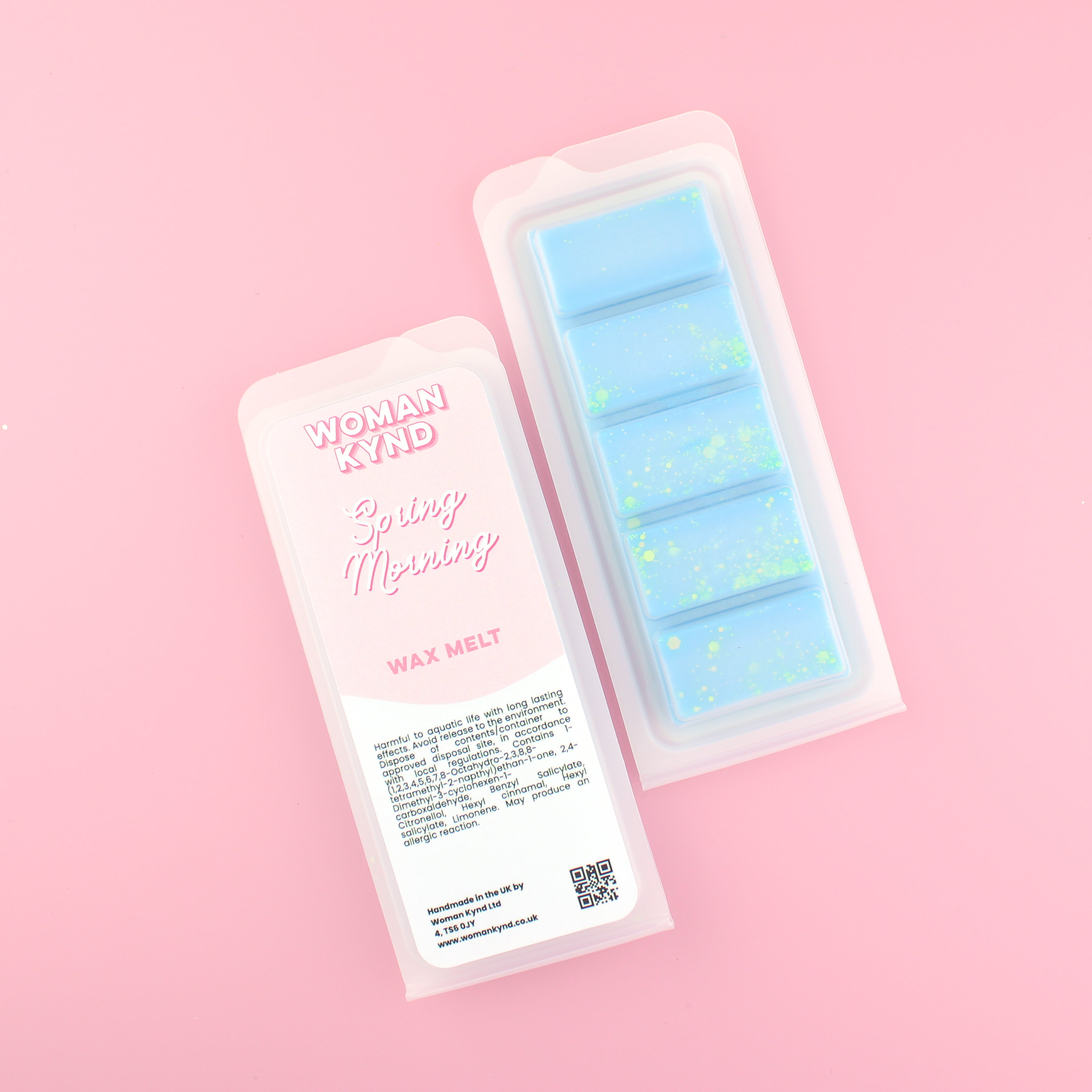 Two images of a Woman Kynd five segment light blue Wax Melt with green glitter, both in a frosted clamshell. The first image displays the pink and white label with the words Woman Kynd Spring Morning Wax Melt and the CLP information, and the other image is of the reverse side showing the Wax Melt Itself. Both images are against a solid pink background.
