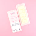Two images of a Woman Kynd five segment off-white Wax Melt with gold glitter, both in a frosted clamshell. The first image displays the pink and white label with the words Woman Kynd Vanilla Buttercream Wax Melt and the CLP information, and the other image is of the reverse side showing the Wax Melt Itself. Both images are against a solid pink background.