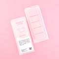 Two images of a Woman Kynd five segment pale pink Wax Melt with gold glitter, both in a frosted clamshell. The first image displays the pink and white label with the words Woman Kynd Vanilla Sugar Wax Melt and the CLP information, and the other image is of the reverse side showing the Wax Melt Itself. Both images are against a solid pink background.